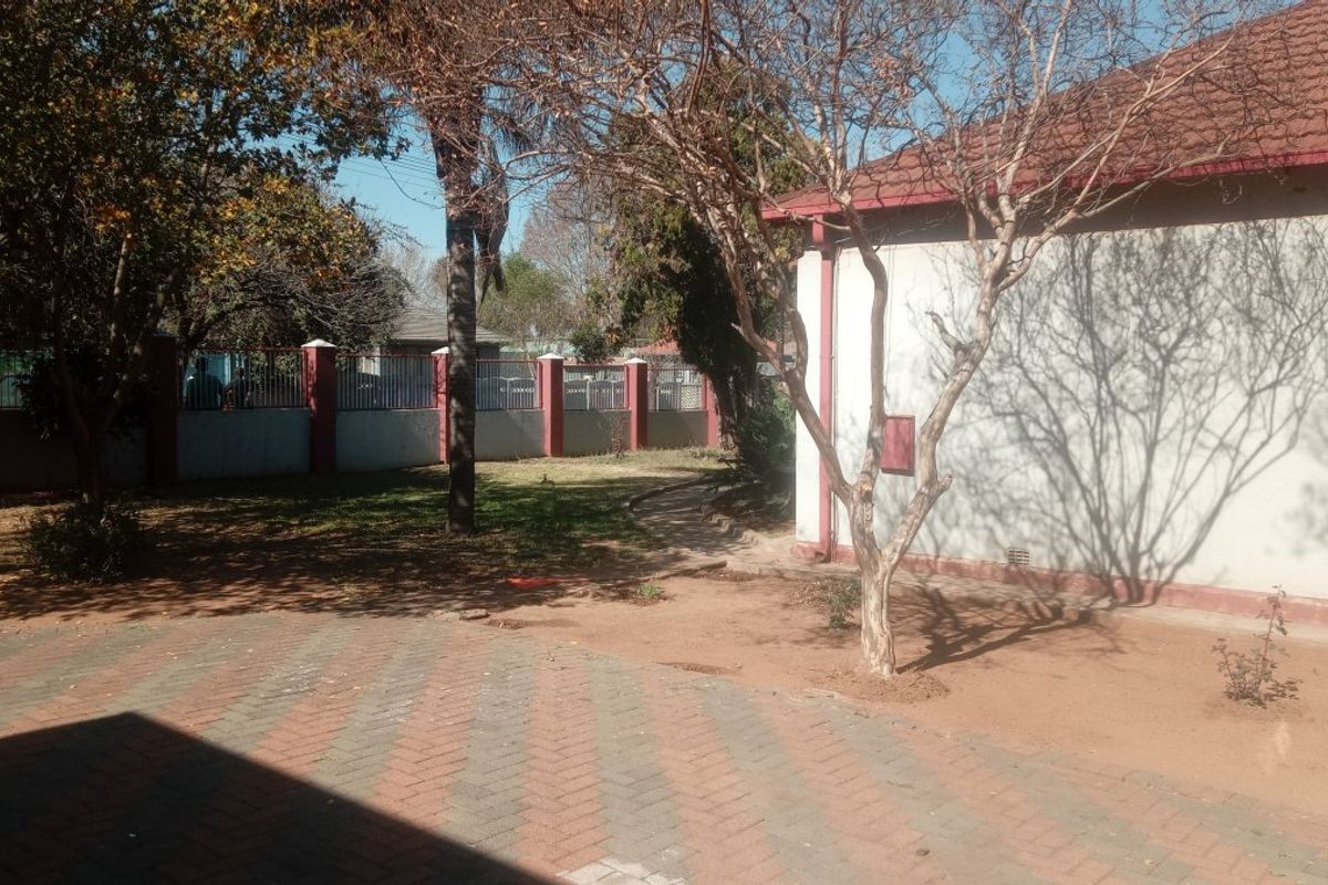 A view of the rear exterior area featuring a paved driveway, perimeter wall with metal fencing, and a tiled roof structure.