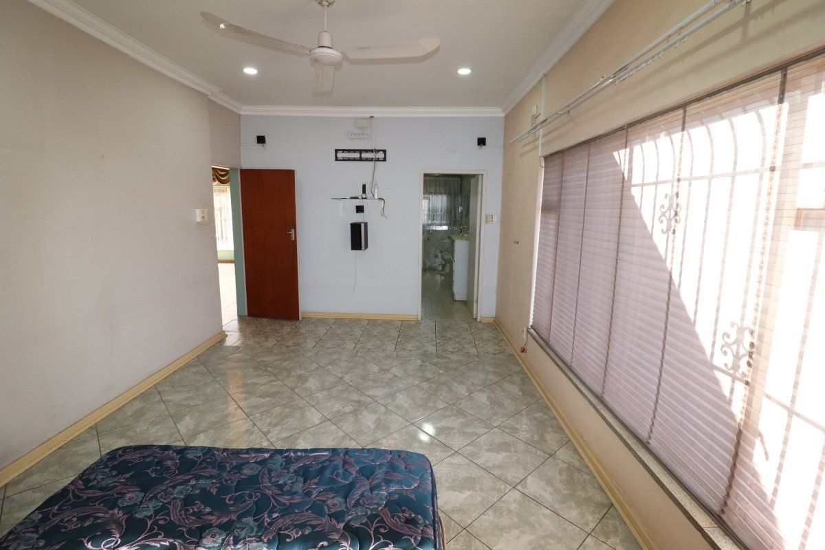 A spacious bedroom featuring tiled flooring, a ceiling fan, and security bars on the windows, offering a blank canvas for potential interior updates.