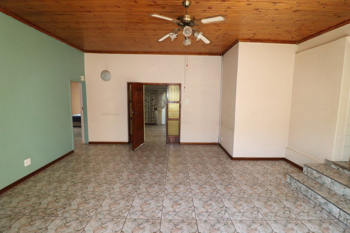 An empty living room featuring a timber ceiling, ceiling fan, and tiled flooring with a small step-up area.