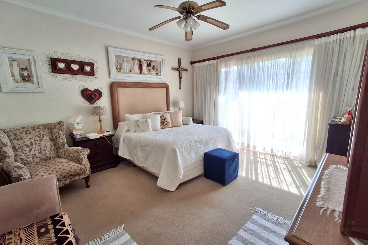 Spacious bedroom featuring a ceiling fan, neutral carpeting, and large windows with floor-to-ceiling curtains allowing for ample natural light.