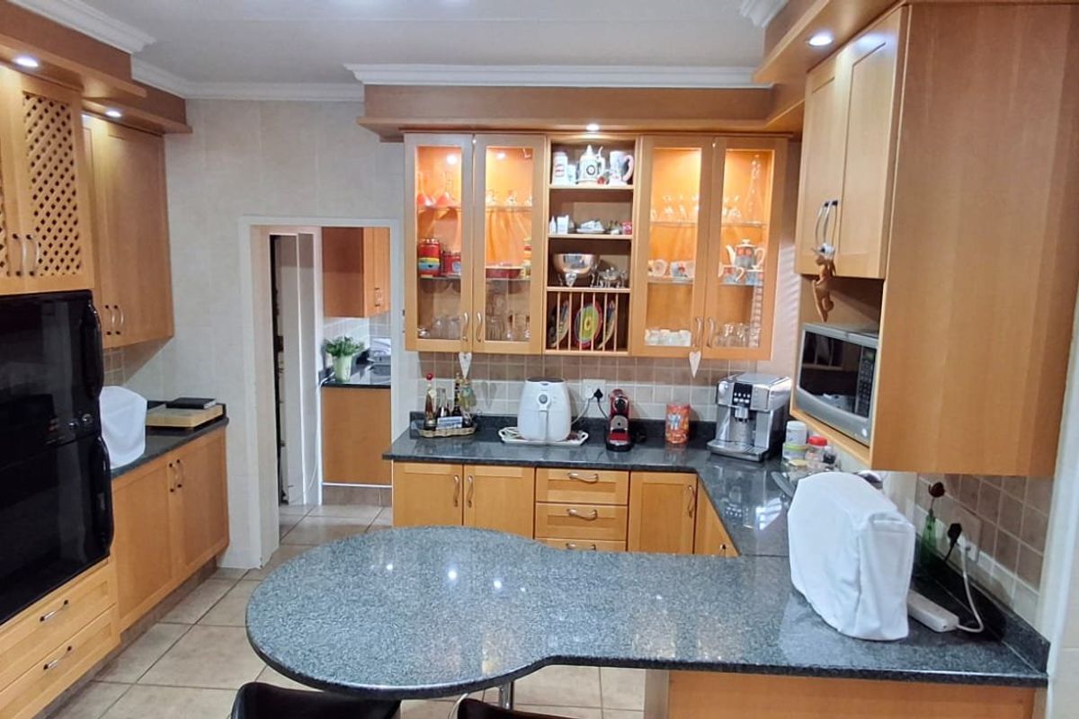A well-maintained kitchen featuring wooden cabinetry, granite countertops, a breakfast bar, and built-in appliances, with a connected scullery area.