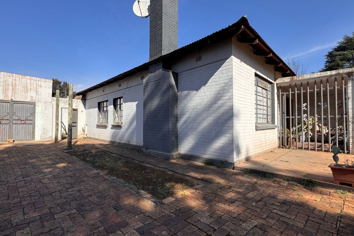 Rear exterior view of the property featuring a brick chimney, paved courtyard area, and security gate access.
