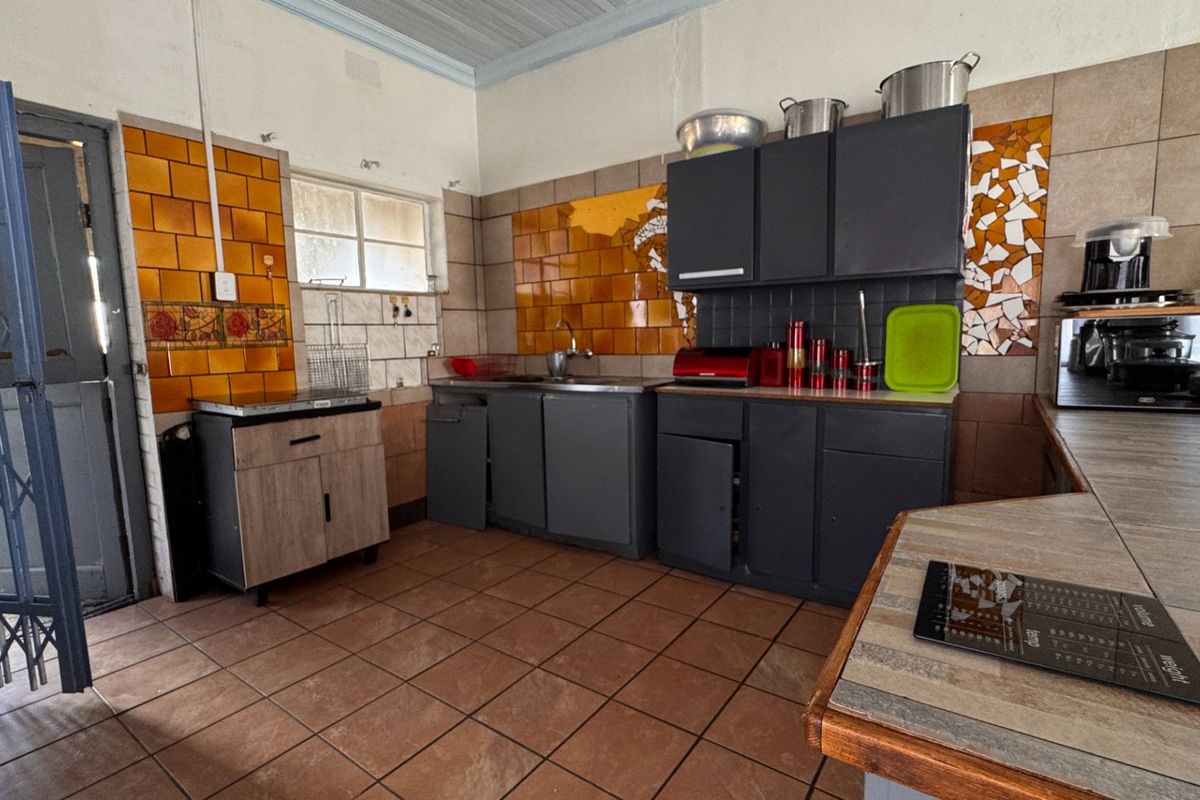 A functional kitchen space featuring tiled flooring, built-in cabinetry, and a tiled splashback, currently requiring cosmetic updates and repairs to cabinetry.
