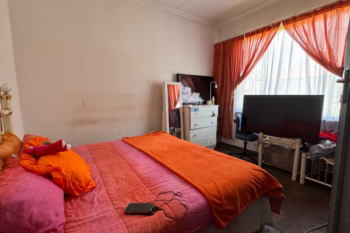 A bedroom featuring a window with security gate and curtain rails, requiring cosmetic updates to the wall finishes.