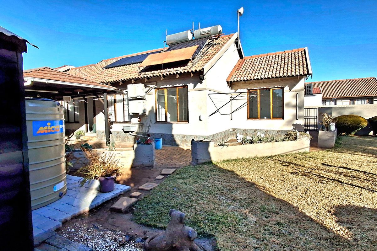 Rear view of the townhouse featuring a paved patio area, solar water heating system, and a private garden with a water storage tank.