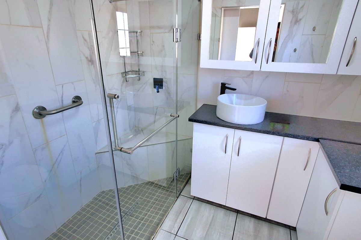 Modern bathroom featuring a glass-enclosed shower, vessel sink vanity with stone countertop, and marble-look wall tiling.