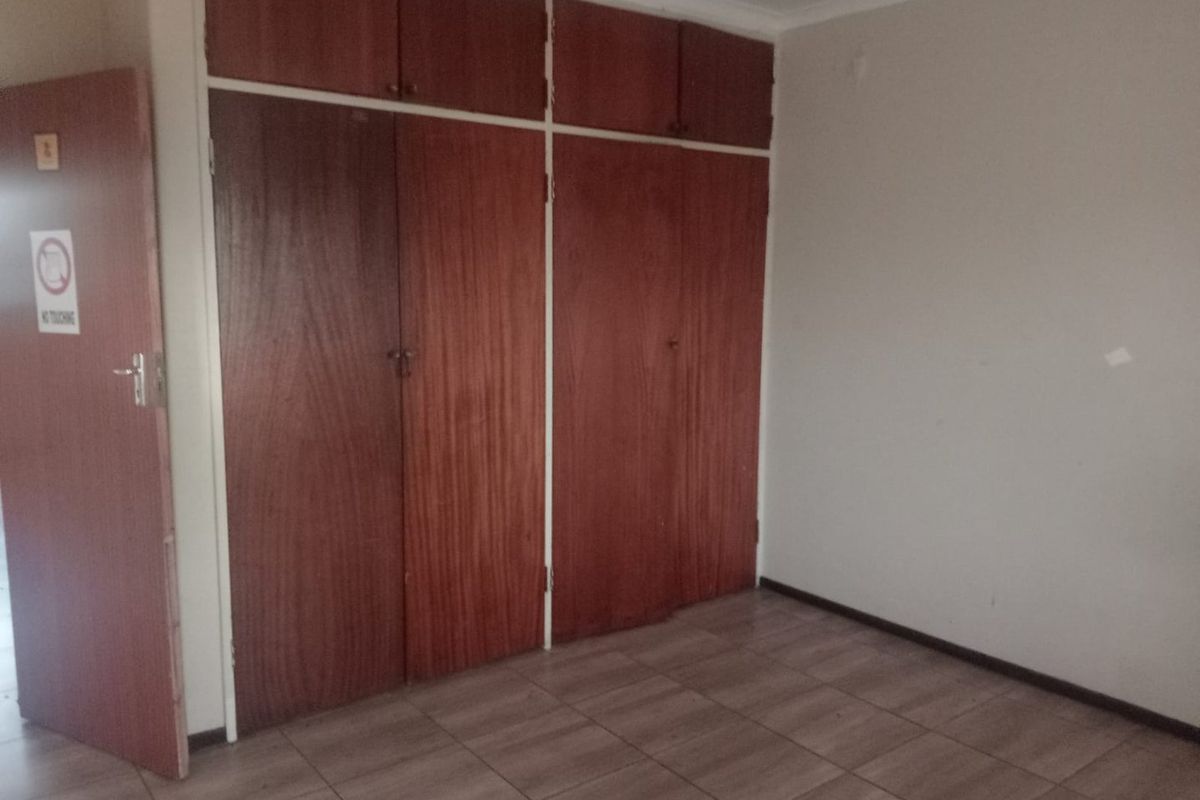An empty bedroom featuring tiled flooring and dated built-in wooden cupboards with overhead storage compartments.