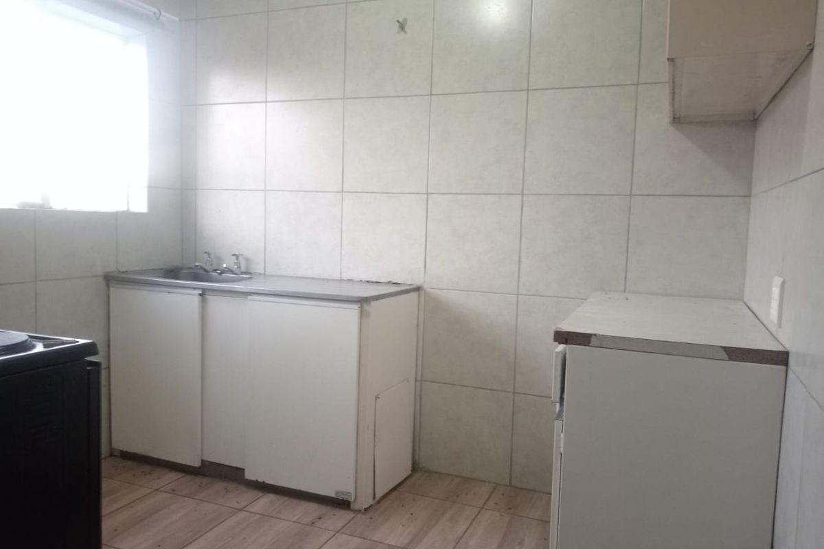 A basic kitchen area featuring tiled walls, a stainless steel sink, and built-in cabinetry, requiring cosmetic updates to improve its overall condition.