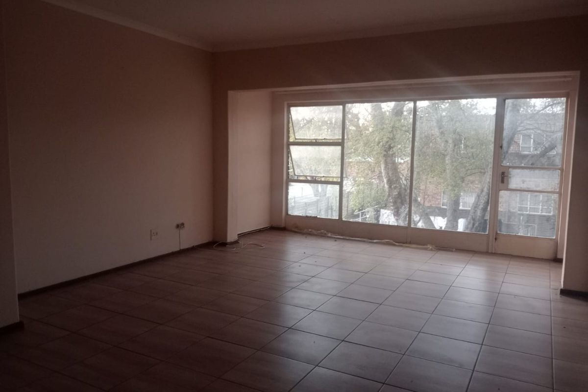 An empty living room featuring tiled flooring and a large window with a glass door, providing natural light and views of the exterior.