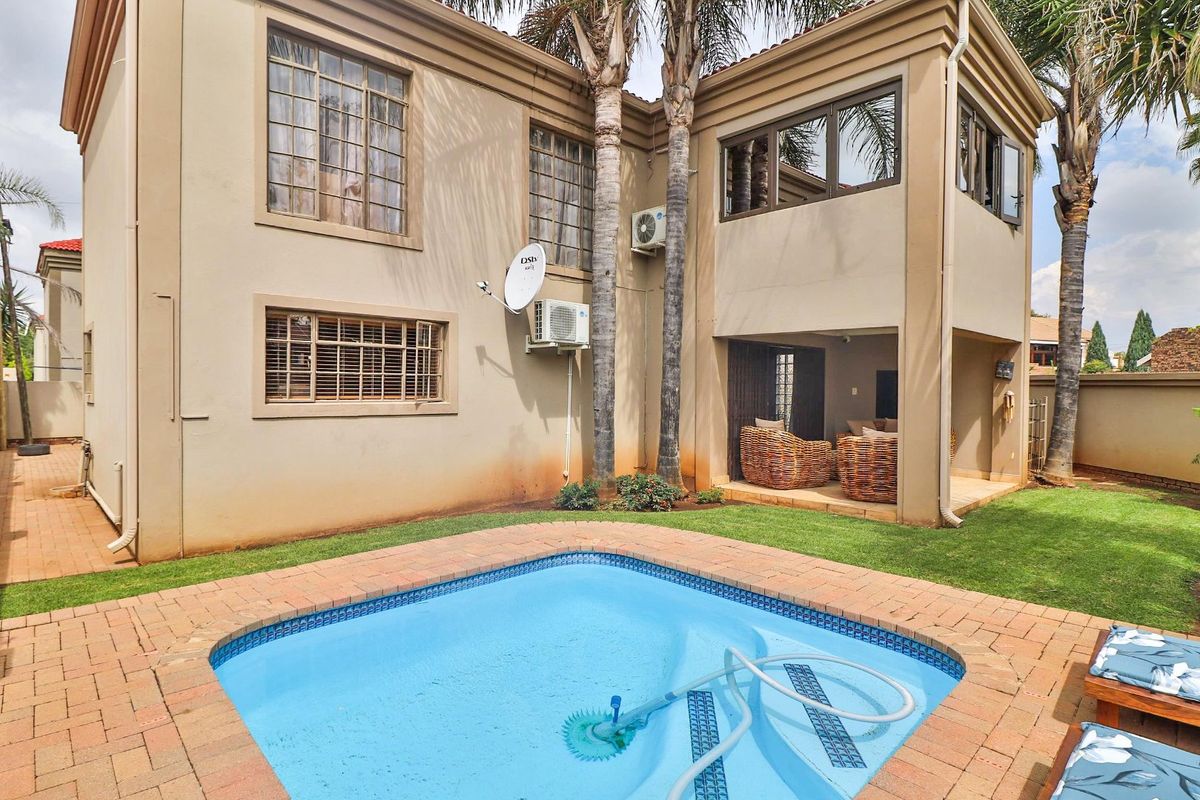 Rear exterior view of the townhouse featuring a swimming pool, brick-paved surround, and a covered patio area.