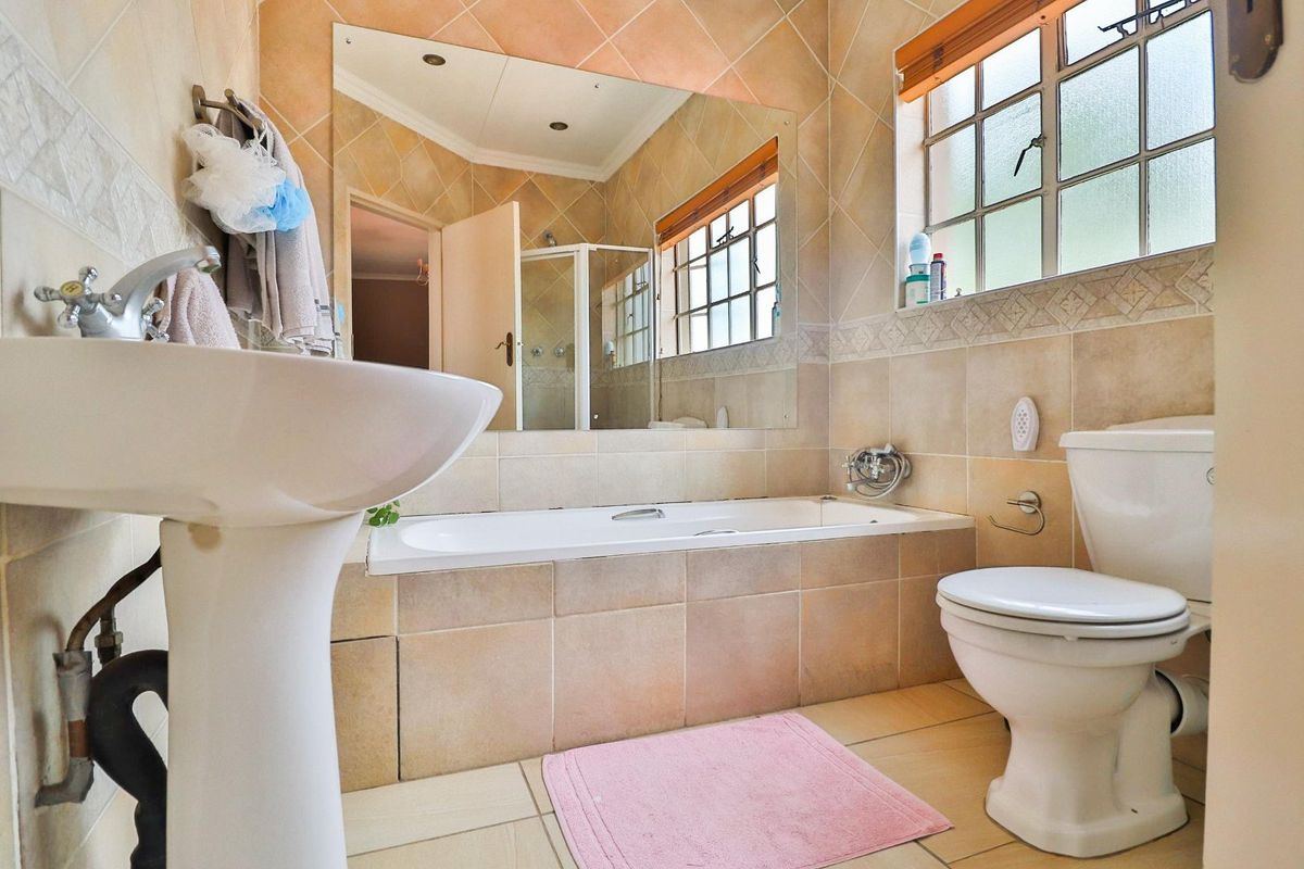 A functional bathroom featuring a pedestal basin, built-in bathtub, toilet, and large wall mirror with neutral tiled finishes.