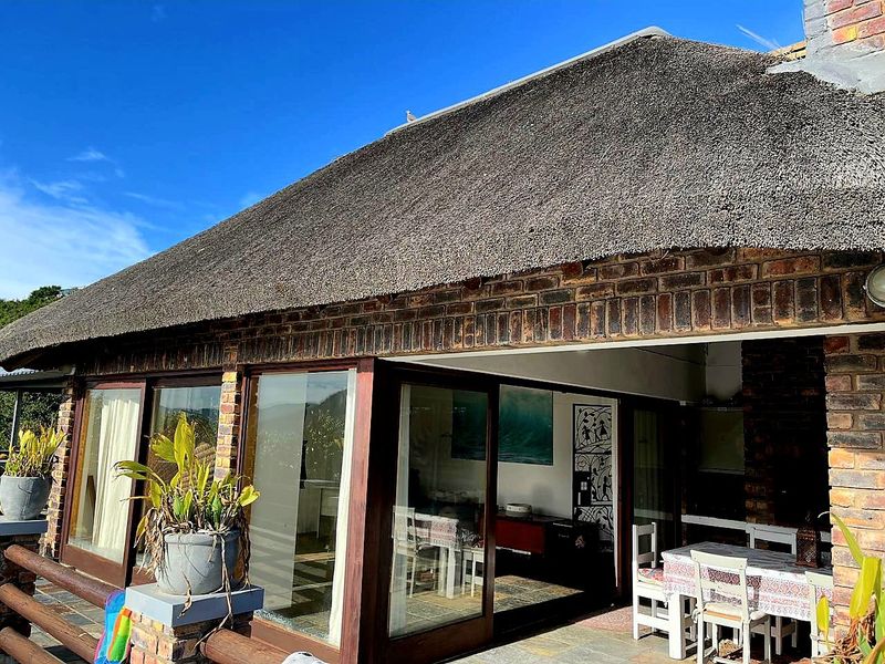 A covered patio area featuring a traditional thatch roof, exposed brick walls, and large sliding glass doors that open into the interior living space.