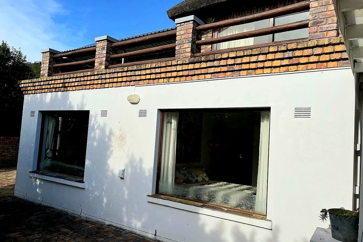 Rear exterior view of the house featuring a paved patio area, white rendered walls, and an upper-level balcony with brick detailing and thatched roofing.