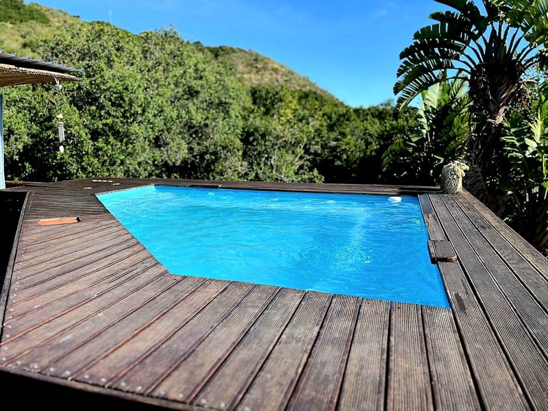 An outdoor swimming pool area featuring timber decking, set against a natural hillside backdrop.