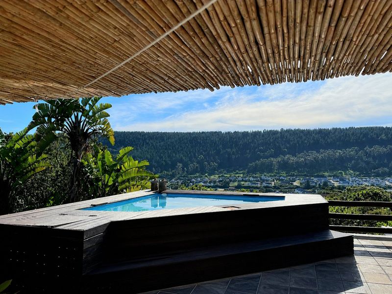 A scenic outdoor pool area featuring a raised timber deck, bamboo pergola, and expansive views of the surrounding landscape.