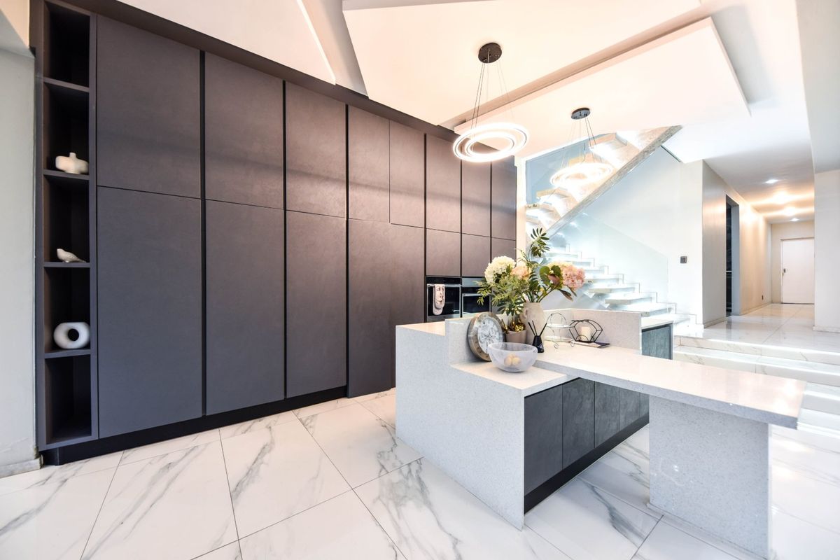 Modern kitchen featuring sleek dark cabinetry, a stone-topped island, and marble-look flooring, seamlessly integrated with a contemporary staircase.