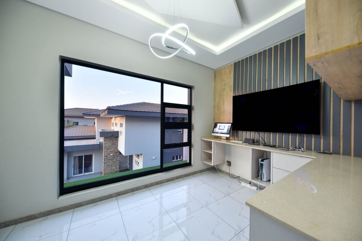 Modern living space featuring high-gloss tile flooring, a custom built-in desk, slatted wood feature wall, and large window with views of the surrounding property.
