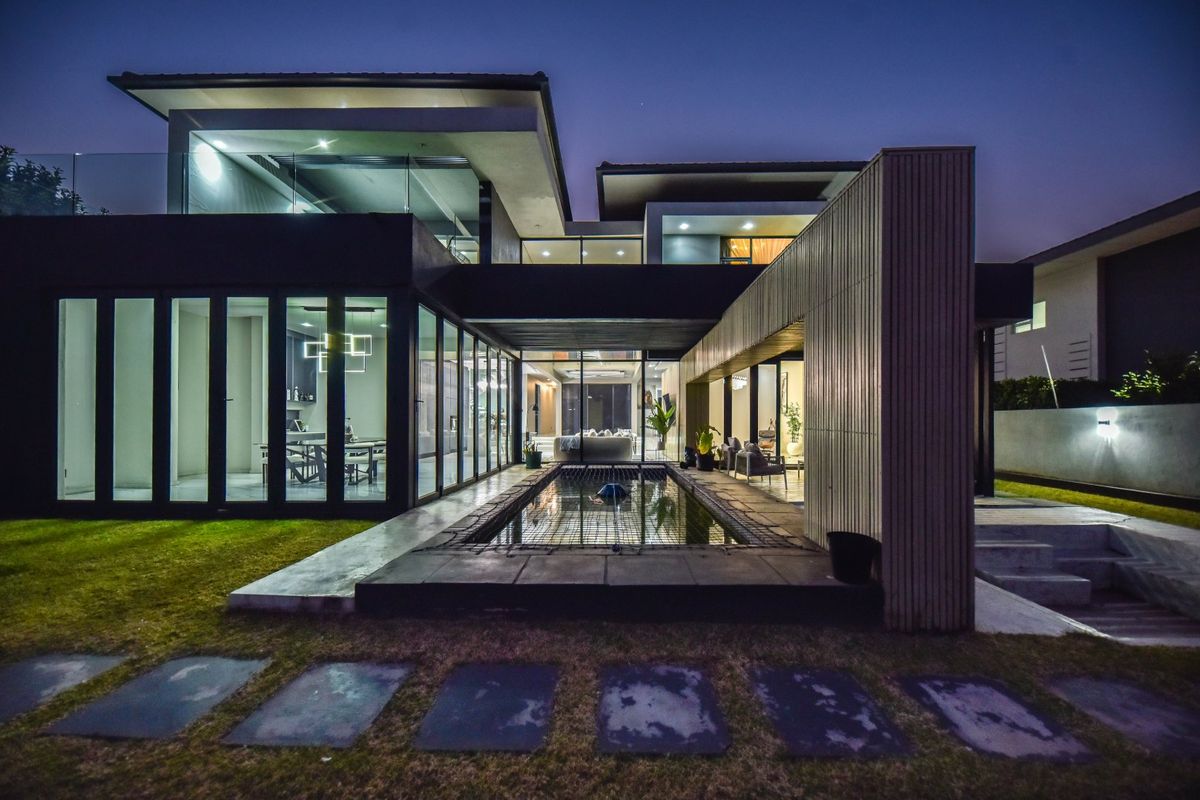 Modern architectural rear elevation featuring a sleek swimming pool, expansive glass sliding doors, and contemporary timber cladding at dusk.