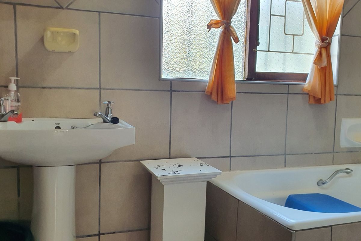 A functional bathroom featuring a pedestal basin, bathtub, and tiled walls, requiring some cosmetic updates to improve its overall condition and aesthetic appeal.