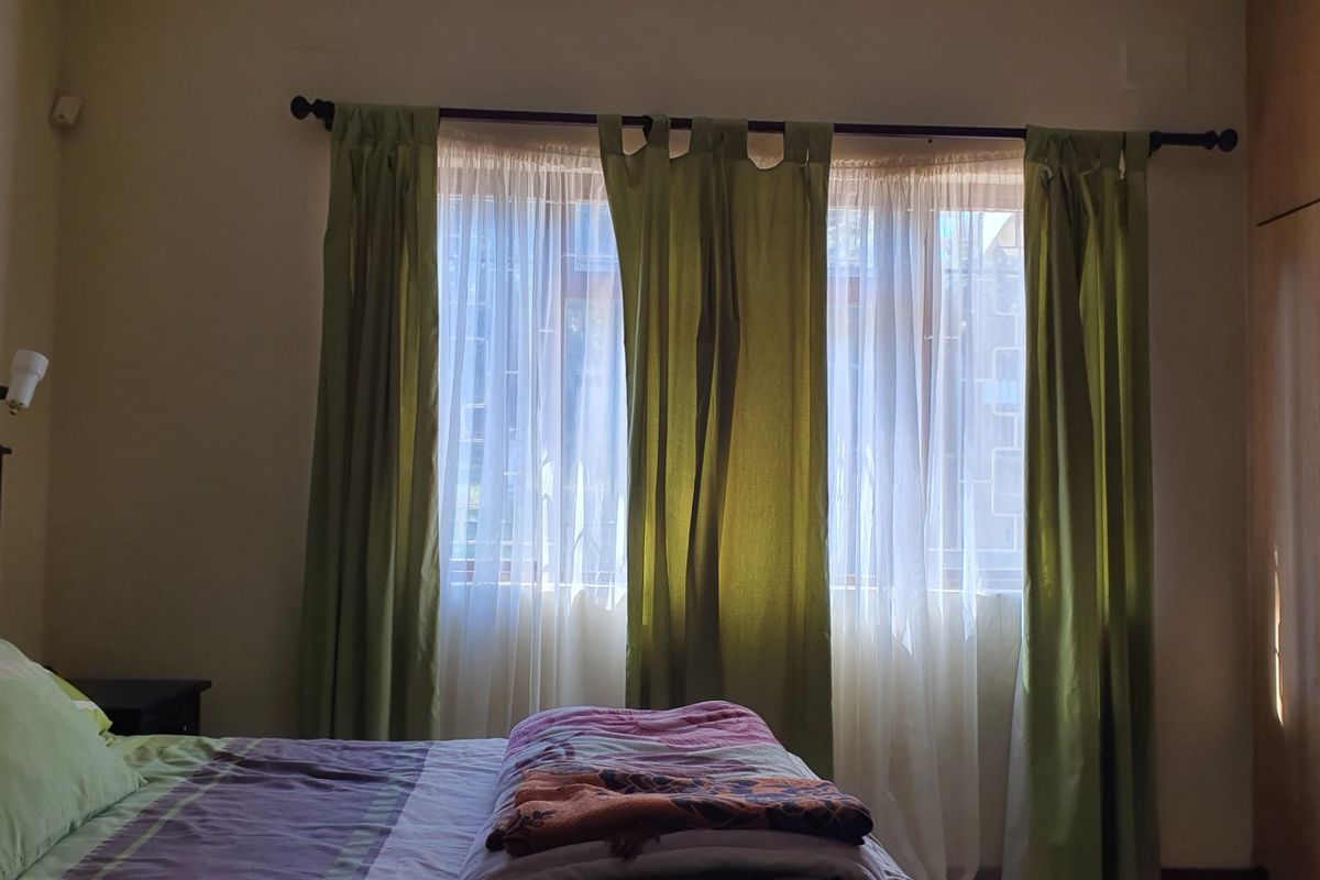 A bedroom featuring a built-in wardrobe, window with security bars, and curtain rod, providing a functional space with natural light.