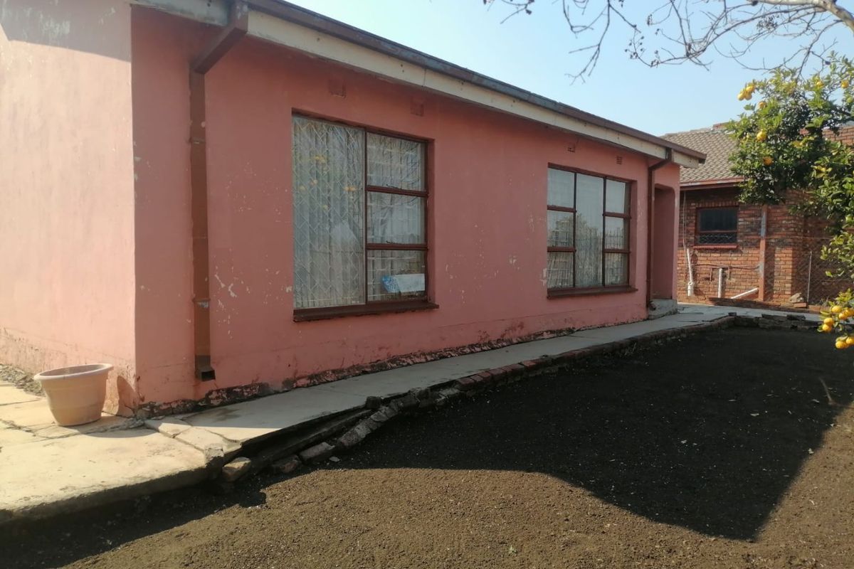 Rear exterior view of the house showing painted masonry walls, metal security window bars, and a concrete pathway requiring maintenance.