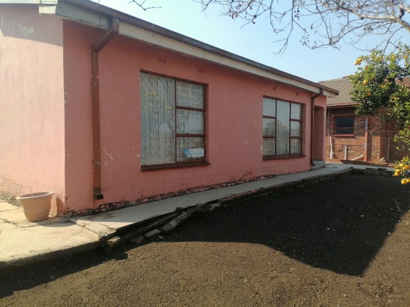 Rear exterior view of the house showing painted masonry walls, metal security window bars, and a concrete pathway requiring maintenance.