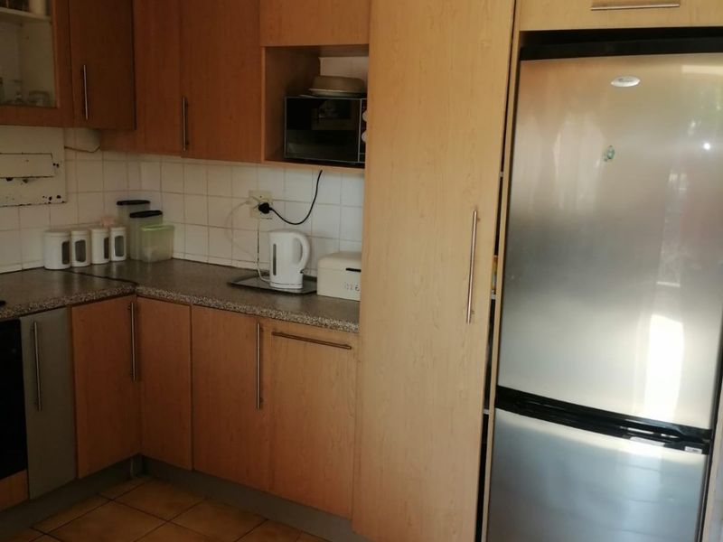 A functional kitchen featuring light wood-tone cabinetry, tiled backsplash, laminate countertops, and ceramic floor tiles, offering a practical layout for daily use.