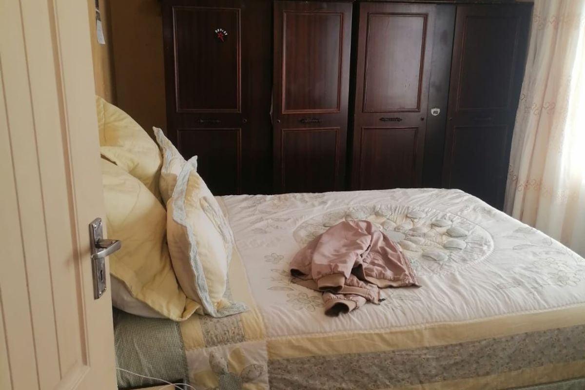 A bedroom featuring dark wood built-in wardrobes and tiled flooring, showing signs of ceiling water damage and wear.