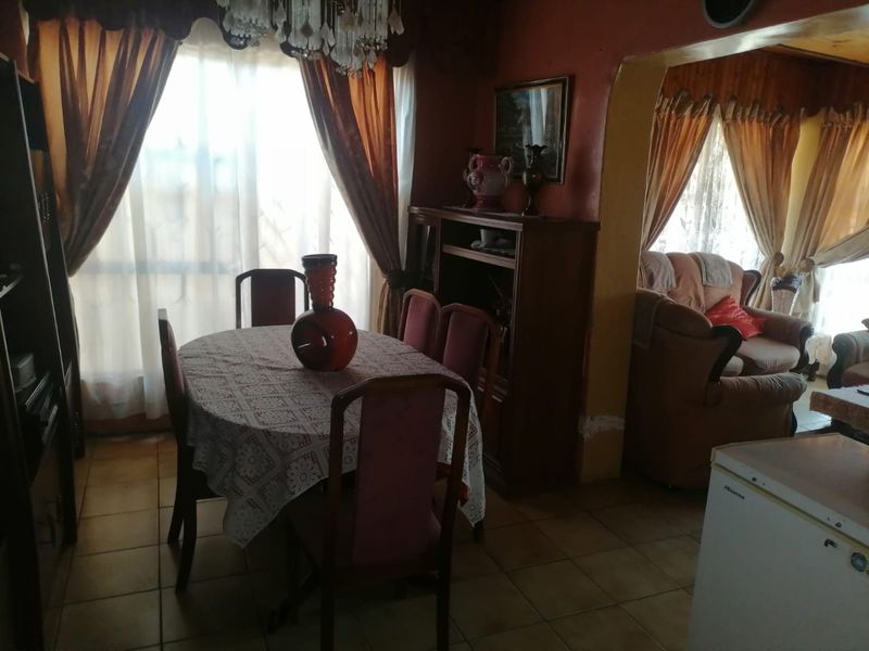 A dining area featuring tiled flooring and an arched transition to the adjacent living space, currently showing signs of wear on the walls.