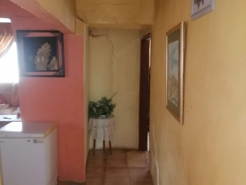 A narrow hallway featuring tiled flooring and visible structural wall cracking, requiring maintenance and cosmetic updates to improve the interior condition.