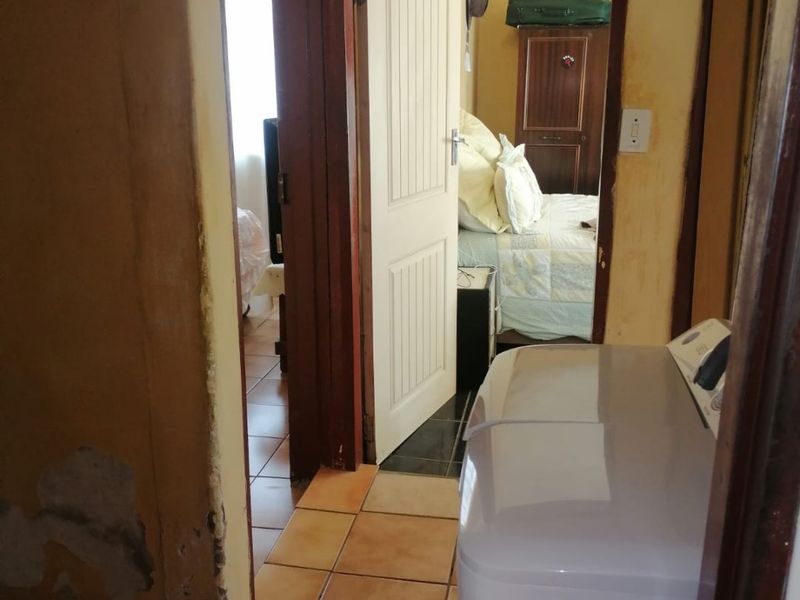 A narrow hallway area showing significant wear to wall finishes and plaster, connecting to adjacent rooms with tiled flooring.