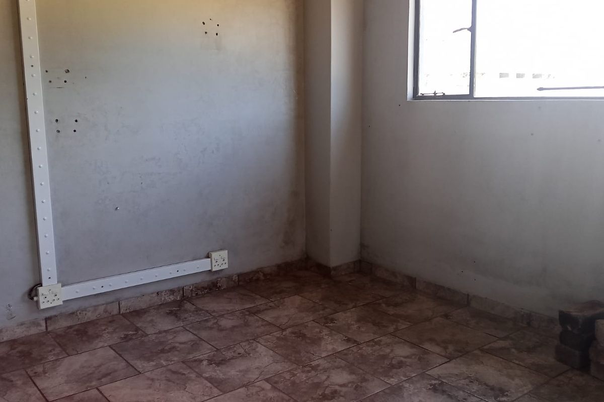 An empty bedroom featuring tiled flooring and surface-mounted electrical trunking, requiring cosmetic updates and wall refinishing to improve its overall condition.
