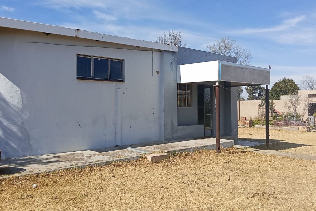 Rear exterior view of the property featuring a concrete patio, covered entrance canopy, and plastered walls showing signs of wear and weathering.