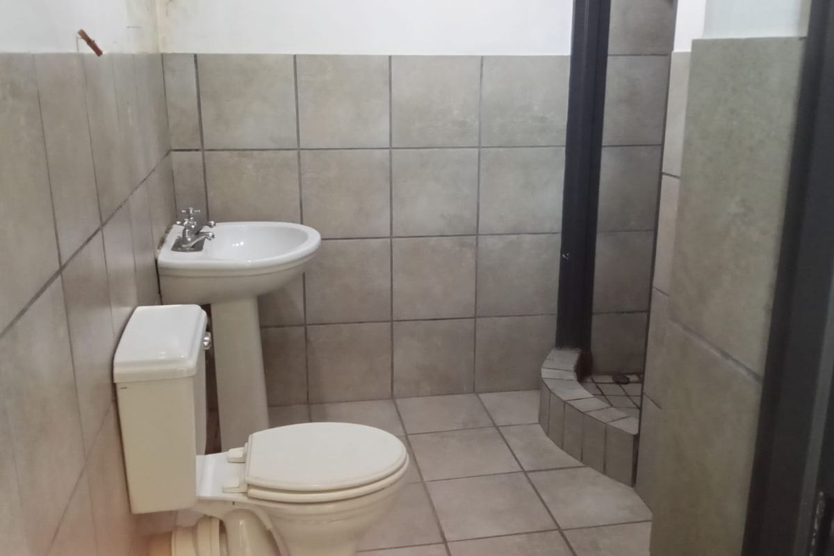 A functional bathroom featuring a pedestal basin, toilet, and a tiled shower enclosure with neutral ceramic wall and floor finishes.