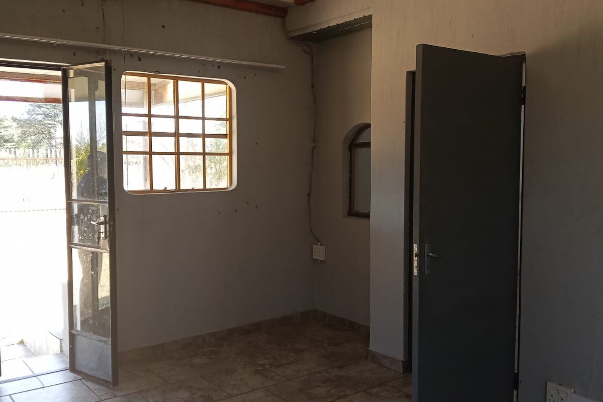An empty living area featuring tiled flooring, steel-framed windows, and direct access to the exterior, requiring cosmetic updates to improve its overall condition.