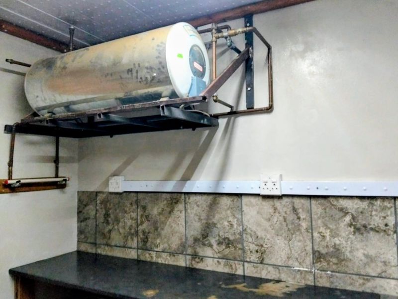 Utility area featuring a wall-mounted electric water heater, exposed copper plumbing, tiled backsplash, and a dark countertop with surface wear.