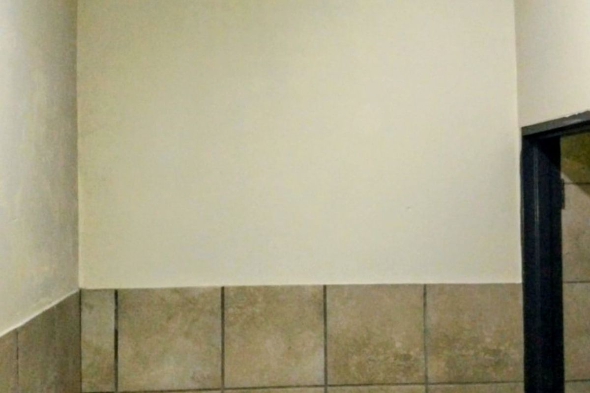 A small bathroom featuring a wall-mounted basin, neutral ceramic wall tiling, and timber ceiling trim, currently in need of cosmetic updates.