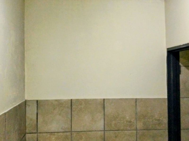 A small bathroom featuring a wall-mounted basin, neutral ceramic wall tiling, and timber ceiling trim, currently in need of cosmetic updates.
