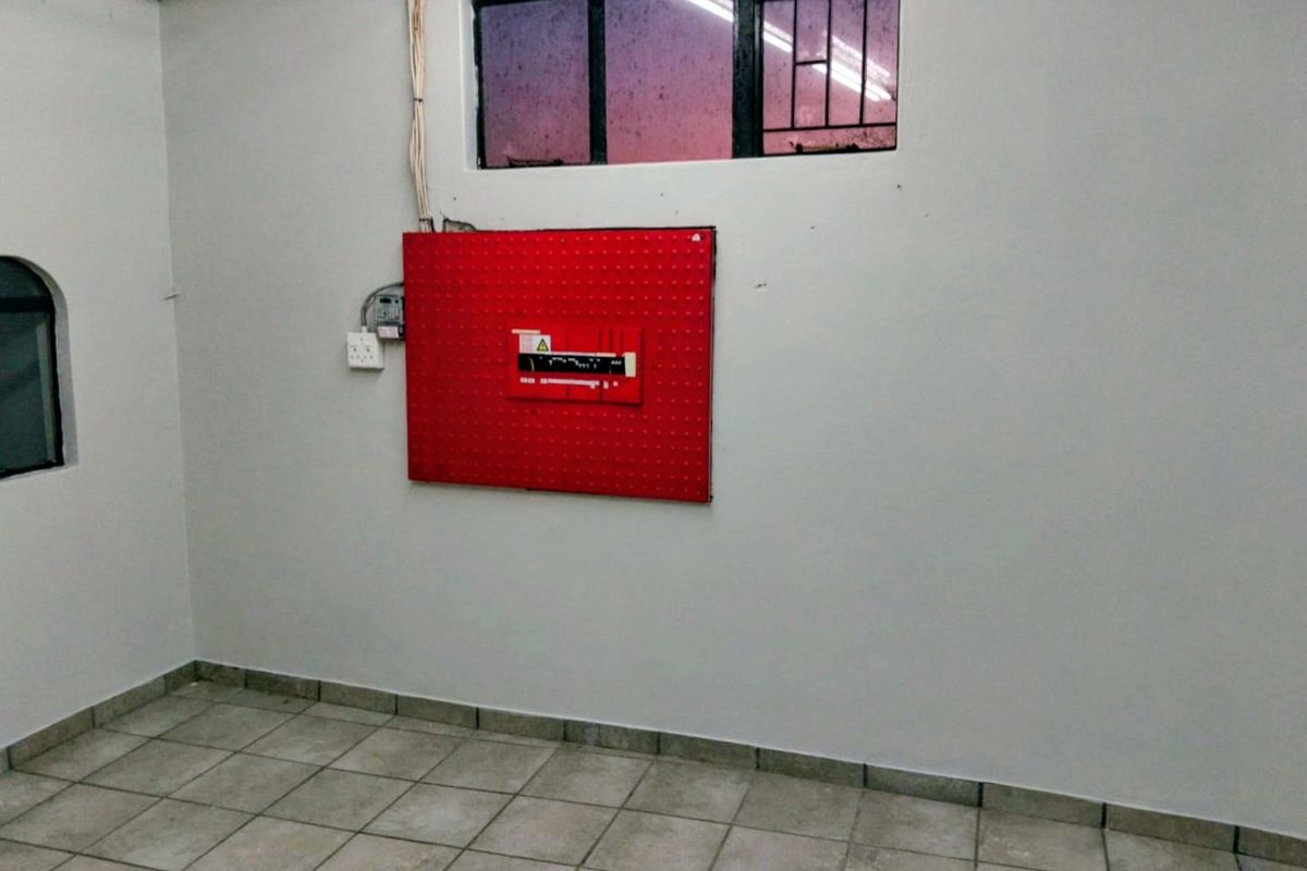 A functional utility space featuring tiled flooring, a wall-mounted electrical distribution board, and security bars on the window.