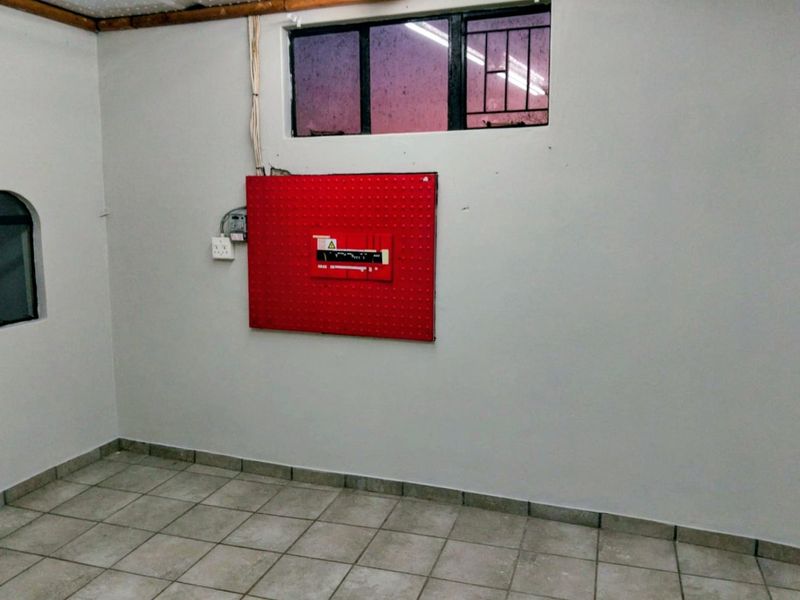 A functional utility space featuring tiled flooring, a wall-mounted electrical distribution board, and security bars on the window.