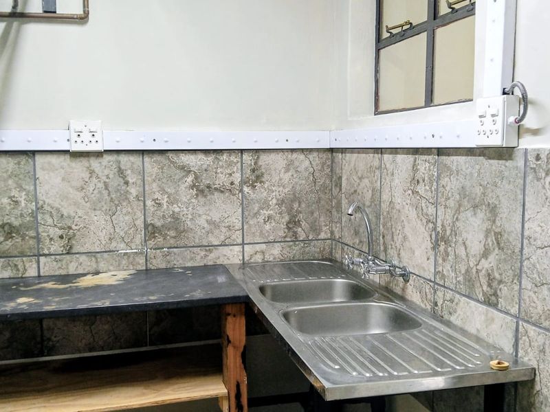 A functional scullery area featuring a double stainless steel sink, tiled splashback, and basic countertop workspace.
