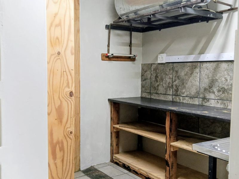 A functional laundry or utility area featuring built-in shelving, a countertop, tiled backsplash, and an integrated sink with exposed plumbing fixtures.