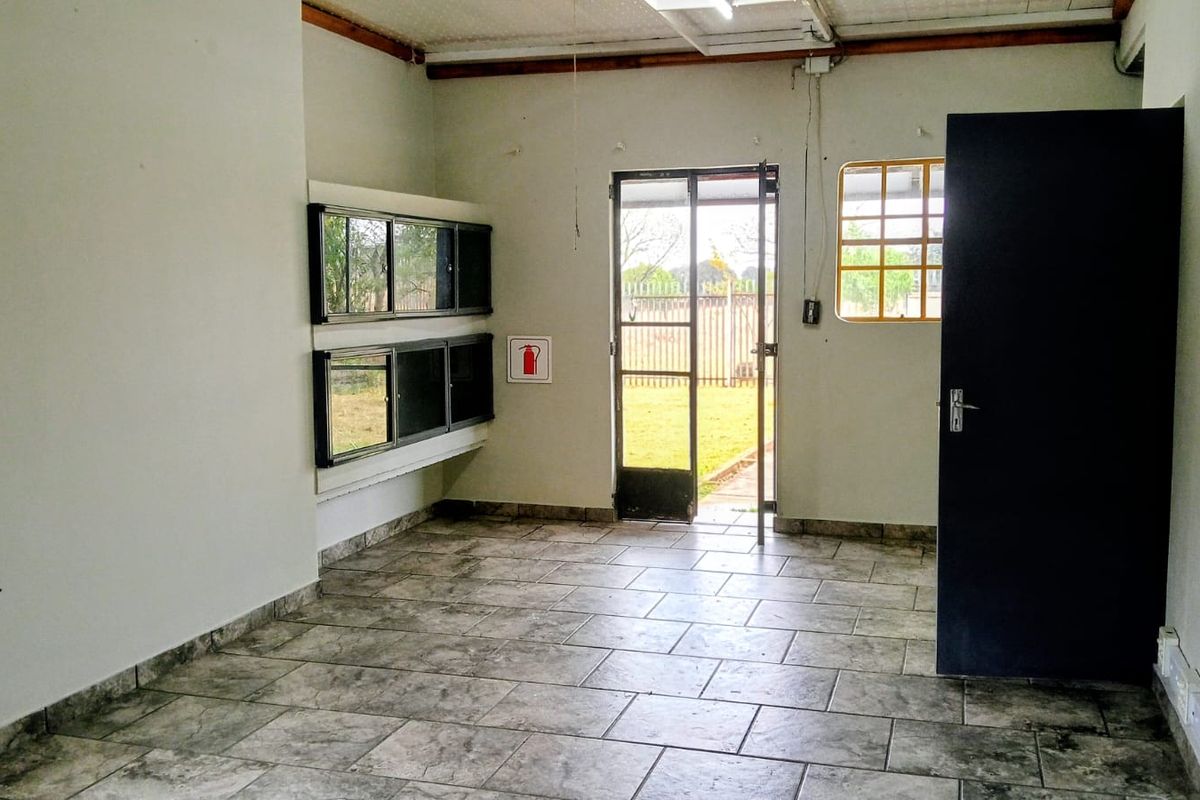 A functional utility space featuring tiled flooring, security gate access to the garden, and exposed ceiling beams, suitable for a laundry or workspace.