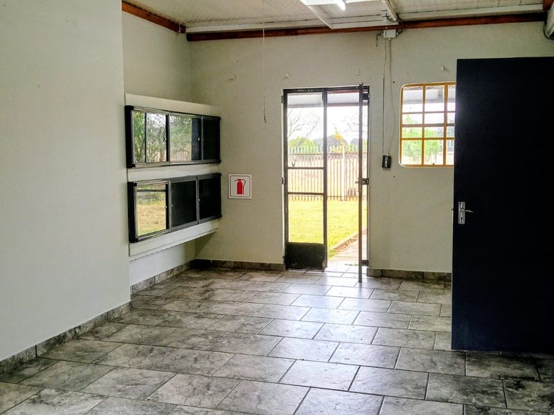 A functional utility space featuring tiled flooring, security gate access to the garden, and exposed ceiling beams, suitable for a laundry or workspace.