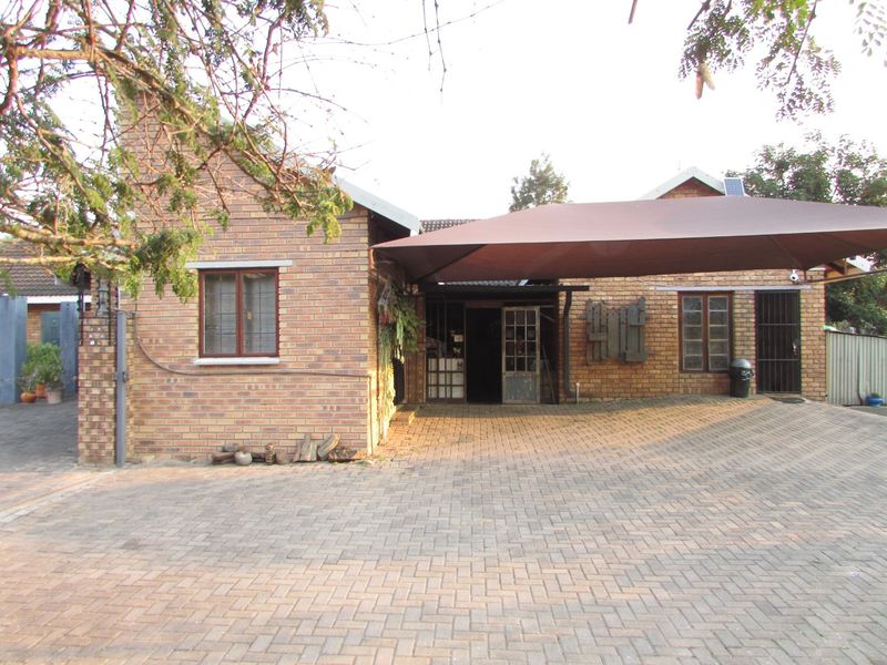Front elevation of a face brick house featuring a paved driveway and a large shade sail carport covering the entrance area.