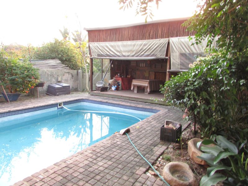 Outdoor pool area featuring a swimming pool, brick paved surround, and a covered patio structure with canvas blinds.