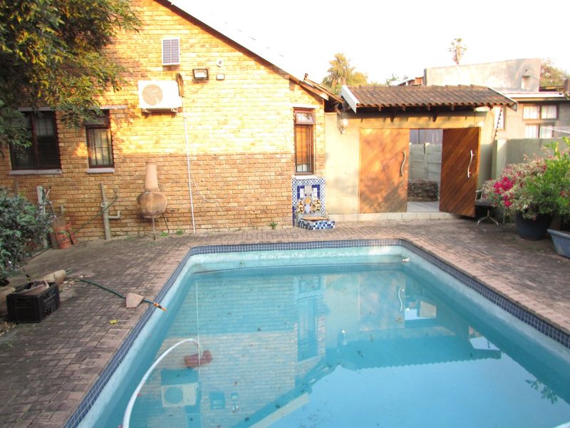 Outdoor pool area featuring a swimming pool, brick paving, and an exposed brick facade with an integrated water feature and wooden gate access.