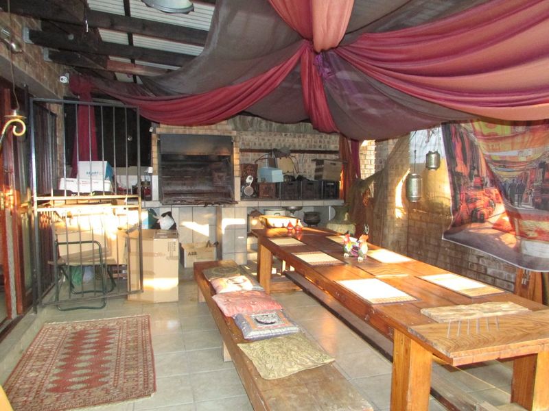 Covered outdoor patio area featuring a built-in braai, exposed timber rafters, and tiled flooring, suitable for outdoor dining and entertainment.