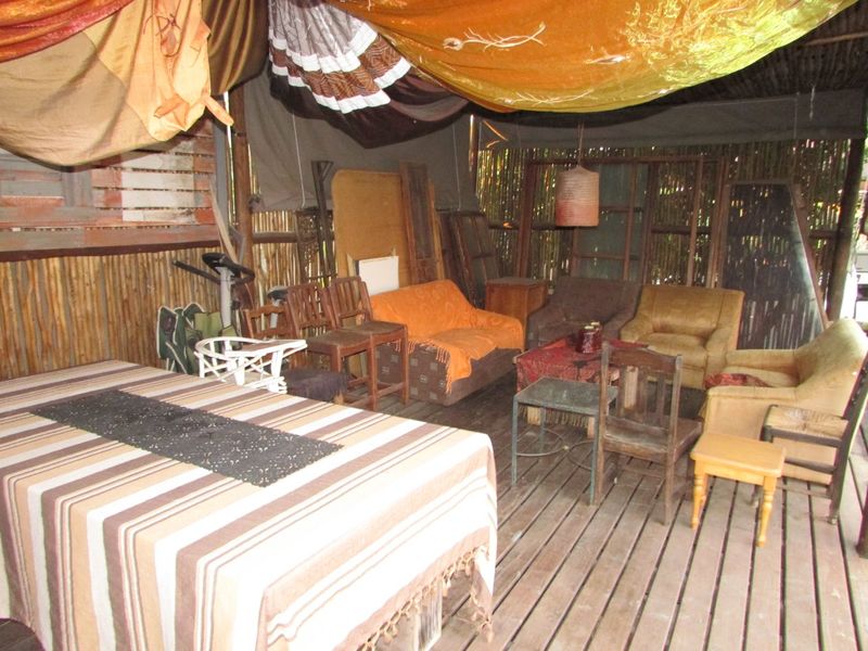 A rustic outdoor patio area featuring timber decking, bamboo wall cladding, and a covered roof structure, offering a casual space for outdoor relaxation.