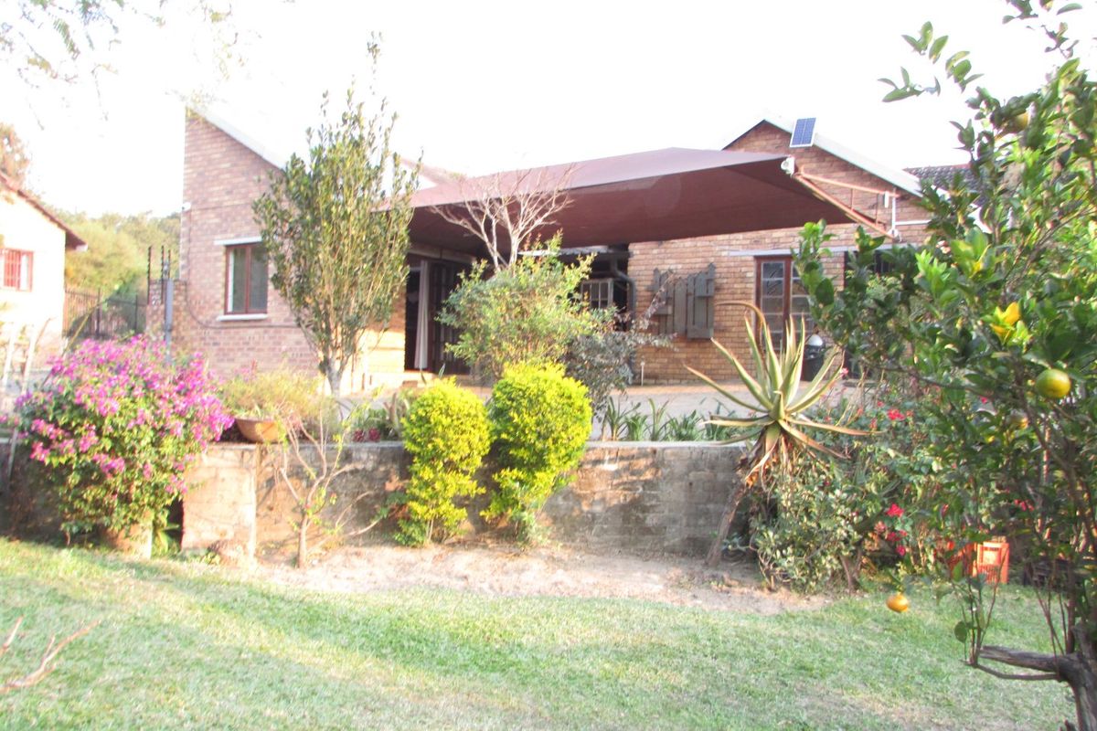 Rear view of a face brick house featuring a large shade sail over the patio area and established garden landscaping.